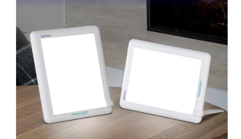 Two Happy Light brand light therapy lamps propped up on a table, one vertical and one horizontal, lit up.